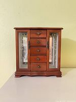Front view of cherry wood jewelry armoire showing five drawers and glass side doors