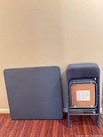 Square blue folding table and stacked matching folding chairs