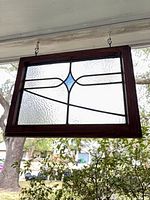 Full view of stained glass panel in wooden frame hanging from hooks