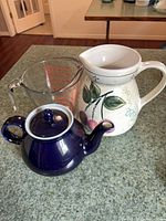 All three items grouped on countertop: glass measuring cup, ceramic floral pitcher, blue ceramic teapot with lid.