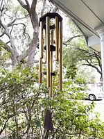 Full view of wind chime hanging outdoors showing six tubes, wood top, clapper, and sail
