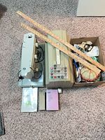 Sewing machine, case, accessories box, yardsticks and booklets on carpet