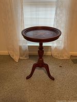 Full view of round wood pedestal side table against window backdrop