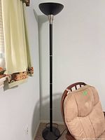 Full view of black torchiere floor lamp beside chair and wall, showing shade, pole, and base