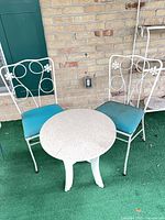 Overall view showing two white metal chairs with teal cushions and round side table
