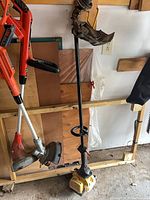 Two orange Black+Decker string trimmers and gas trimmer hanging on rack