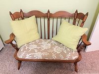 front view of wooden two-seat settee with floral cushion and two green pillows