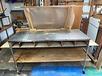 Front view showing stainless top, six cubbies, mid and lower shelves, and casters