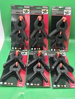 Six retail packets of two-count plastic spring clamps on green background