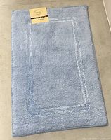 Full view of Alkaso 20 x 30 in light blue bathmat showing color, border design and attached product label