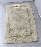 Full view of Alkaso beige shag bathmat with factory label displayed