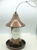 Full view of bird feeder showing lid, glass tube, base and hanging wire