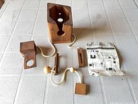 All puzzle components laid out: hexagonal sleeve, two blocks, rope with beads, flat piece, instruction sheet