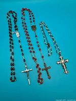 Full view of three bead necklaces each ending in a crucifix or cross