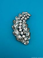Front view of rhinestone leaf brooch on blue background