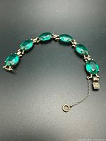 Full view of sterling silver bracelet showing six green stones and safety chain