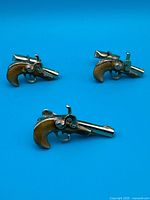 Front view of all three gold-tone flintlock pistol accessories