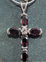 Front view of silver cross pendant with garnets on chain