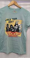 Front view of light teal Aerosmith World Tour 2007 graphic T-shirt on hanger