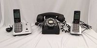 Group shot of black rotary phone centered between two VTech cordless handsets with bases and cords