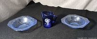 Front view of three cobalt glass items: creamer with portrait between two etched bowls