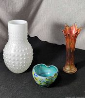 Group shot of three glass pieces: milk glass hobnail vase, carnival glass vase, multicolor art glass bowl