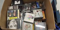 Open box filled with assorted CD jewel cases, visible titles and artwork