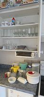 Open cabinet showing drinkware on shelves and assorted kitchen items on countertop