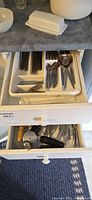 Two drawers open showing stainless flatware in tray above and assorted utensils below