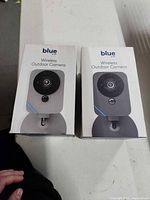 Front view of both boxed ADT Blue wireless outdoor security cameras