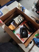 Cardboard box with stapler, hole punch, label maker and tape dispenser visible