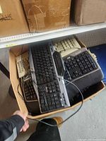 Open cardboard box filled with multiple wired computer keyboards