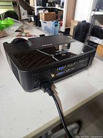 Rear view showing ports (VGA, HDMI, USB-B, composite, audio) and power cord connection