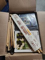 Open box showing wooden rug frame parts, patterned latch-hook canvas, sealed kit and mesh pieces