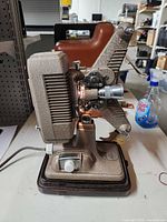 Side view of Revere P-90 projector showing lens, reel arms, base, and power cord