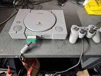 Front view of Sony PlayStation console with memory card inserted and controller attached