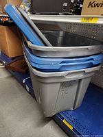 Two stacked grey plastic totes with blue lids on shelf