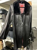 Front view of black leather coat hanging, showing fur collar