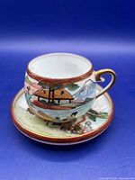 Teacup on saucer showing exterior scenic painting, gold rim and handle