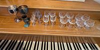 All 20 pieces lined up on piano: silver chalices, teal goblet, blue stem glasses, etched liqueur glasses, 12 French crystal pieces.