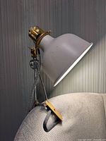 Full view of lamp clamped to furniture showing shade, arm, clamp and cord