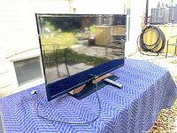 Front three-quarter view of Samsung TV on stand with power cord and remote visible