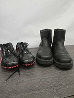 Pair of black/red athletic cleats next to black leather ankle boots