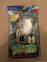 Front view of sealed Angela Spawn Deluxe Edition figure showing accessories and card