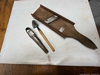 Top-down view of all three vintage tools: wooden mandoline slicer, metal bulb planter, garden trowel