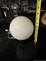Lamp assembled showing spherical white glass shade with tape measure indicating height