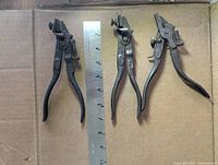 Overall view of three saw set pliers beside ruler for scale