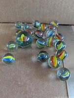 Group of twenty-one glass cat’s eye marbles including one larger shooter displayed on cardboard