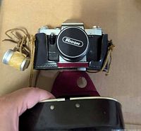 Front view of Praktica LB2 with Ricoh lens cap fitted, leather case attached, film canister to left