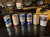 front view of six vintage pull-tab beer cans on table